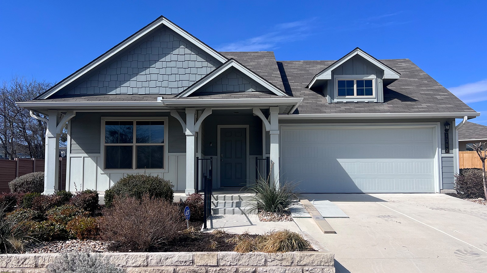 View of front of house with concrete driveway, a shingled roof, and covered porch