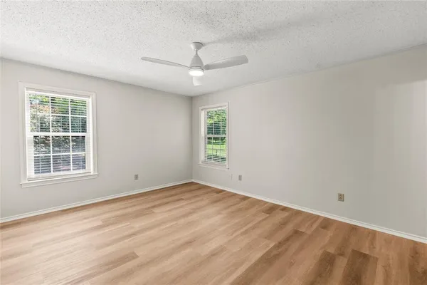 an empty room with wooden floor ceiling fan and windows