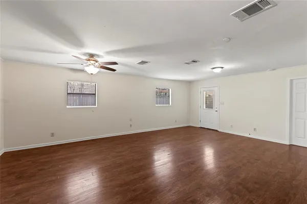 an empty room with wooden floor chandelier fan and windows