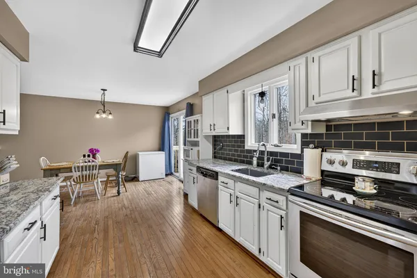 a kitchen with stainless steel appliances a stove a sink dishwasher and white cabinets with wooden floor