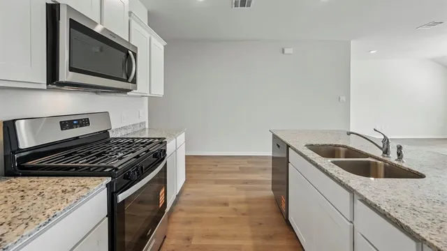 a kitchen with stainless steel appliances granite countertop a stove top oven a sink a refrigerator and white cabinets with wooden floor