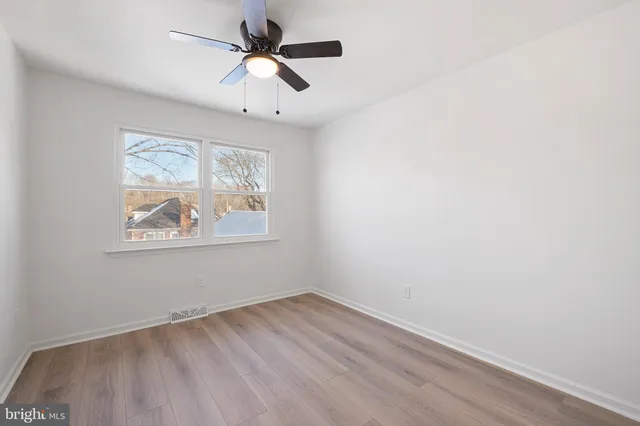 an empty room with wooden floor ceiling fan and windows