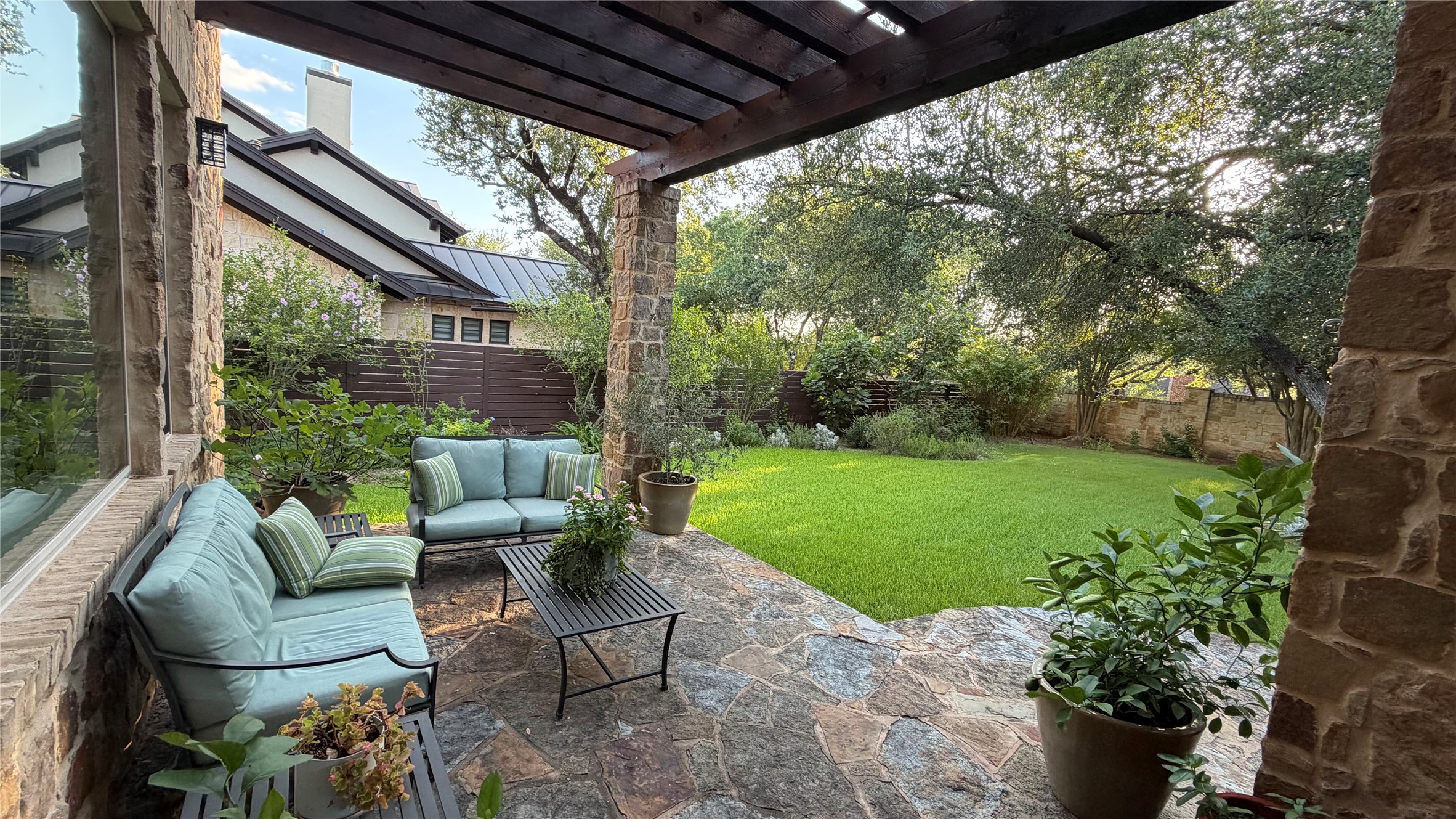 816 Stonewall Ridge Lane Austin, TX 78746 - Photo 6 of 32 Cool seating area beneath a wooden pergola offers a tranquil setting overlooking the lush, verdant lawn.