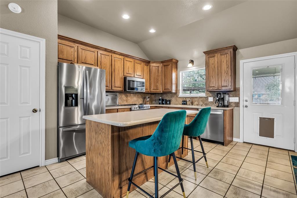 226 King George Road Ponder, TX 76259 - Photo 23 of 39 Kitchen featuring a kitchen island, a kitchen bar, brown cabinets, vaulted ceiling, and decorative backsplash
