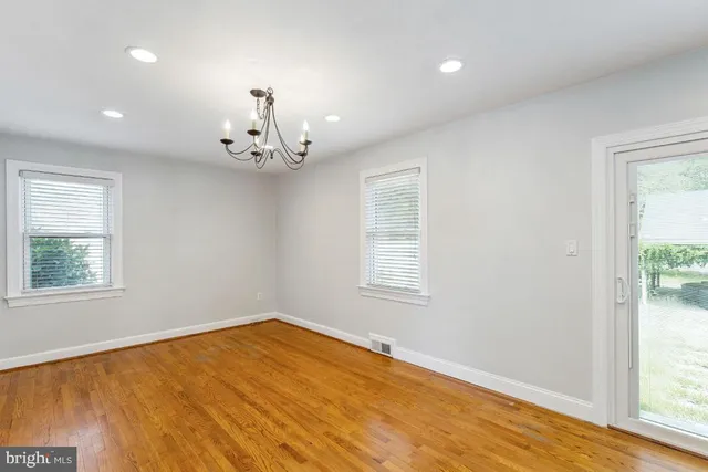 an empty room with wooden floor chandelier and windows