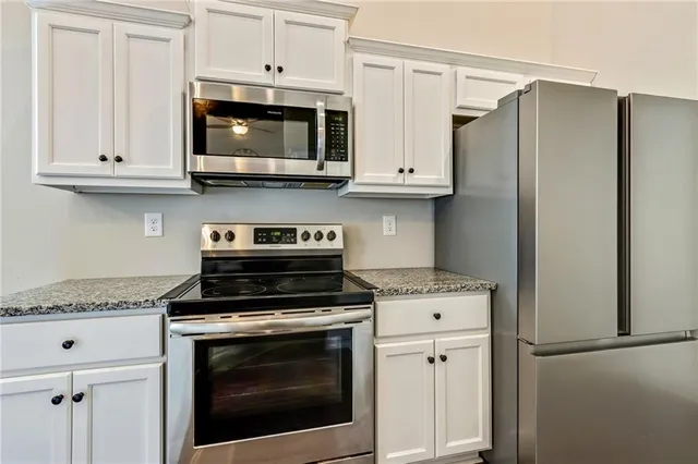 a kitchen with stainless steel appliances granite countertop white cabinets and a stove a refrigerator with wooden floors
