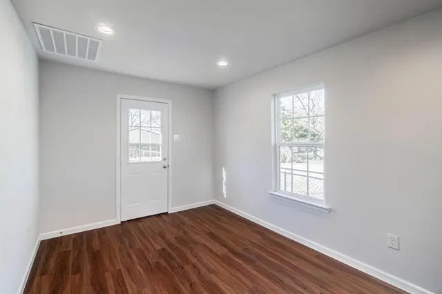 a view of an empty room with wooden floor and a window