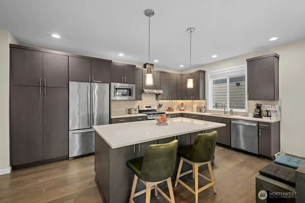 a kitchen with stainless steel appliances granite countertop a sink a stove a refrigerator and island with wooden floor