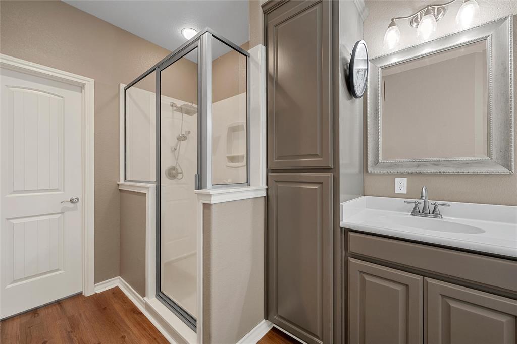 1117 Downsville Road Robinson, TX 76706 - Photo 19 of 40 Bathroom featuring a glass-enclosed shower, wood-finish flooring, a single vanity with a white countertop, a framed mirror, and a tall built-in storage cabinet