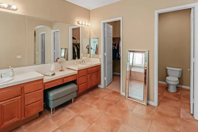 a spacious bathroom with a double vanity sink a large mirror and a toilet