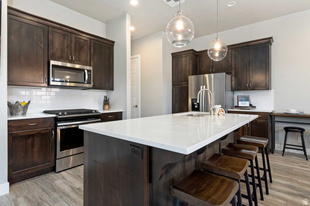 2600 Ocotillo Way, Unit 31 Santa Clara, UT 84765 - Photo 11 of 73 Kitchen featuring a large central island with a light-toned countertop, dark wood-finish cabinetry, stainless steel appliances, a white subway tile backsplash, and wood-look flooring