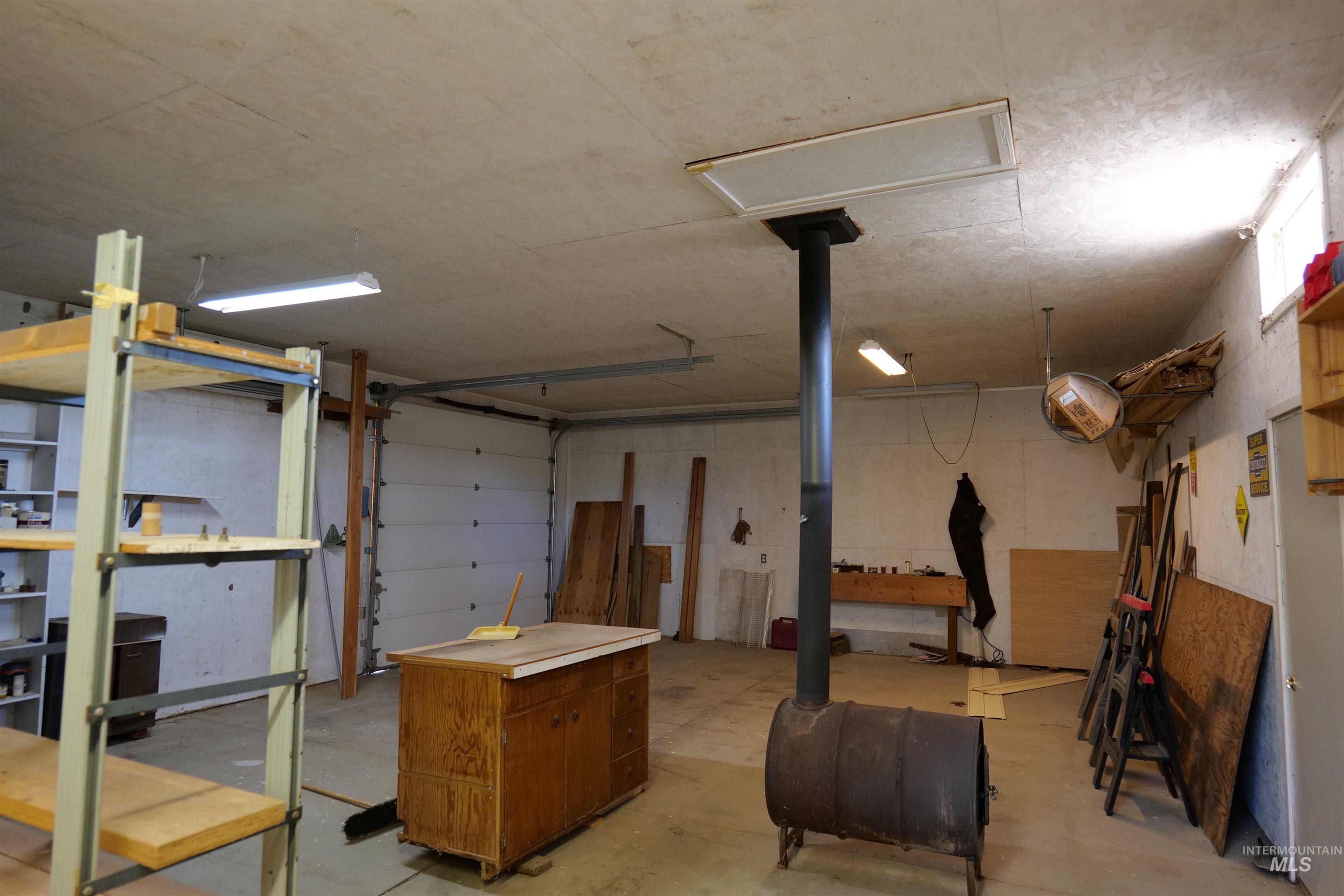 1485 East 9th Street Weiser, ID 83672 - Photo 15 of 18 Spacious shop interior featuring concrete flooring, a large overhead door, fluorescent lighting, and a drum stove with an exhaust pipe