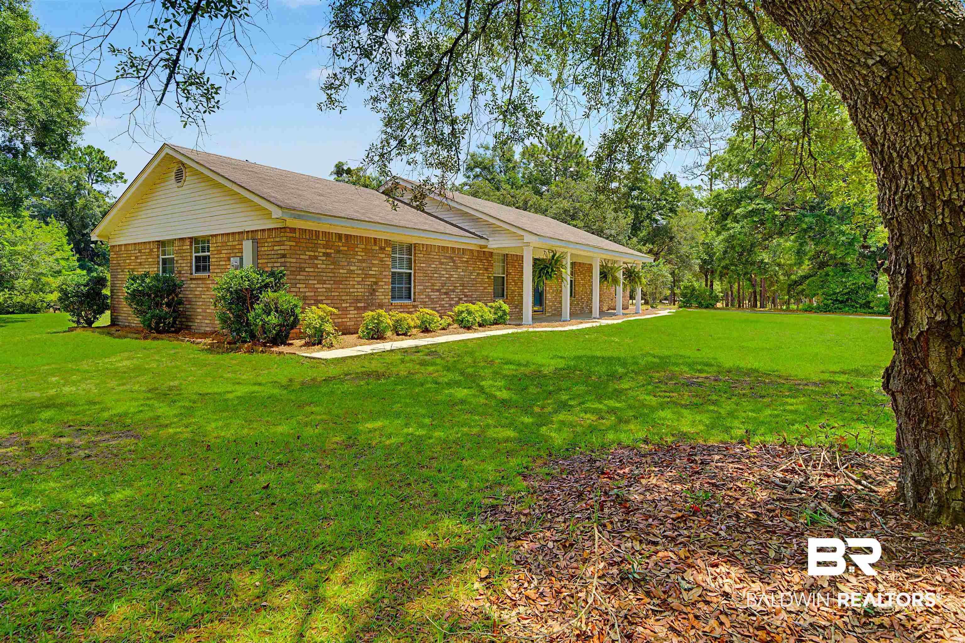 22963 Highway 98 Foley, AL 36535 - Photo 5 of 52 Brick exterior featuring a covered porch with white columns, a meticulously maintained lawn, mature landscaping, and a surrounding wooded area