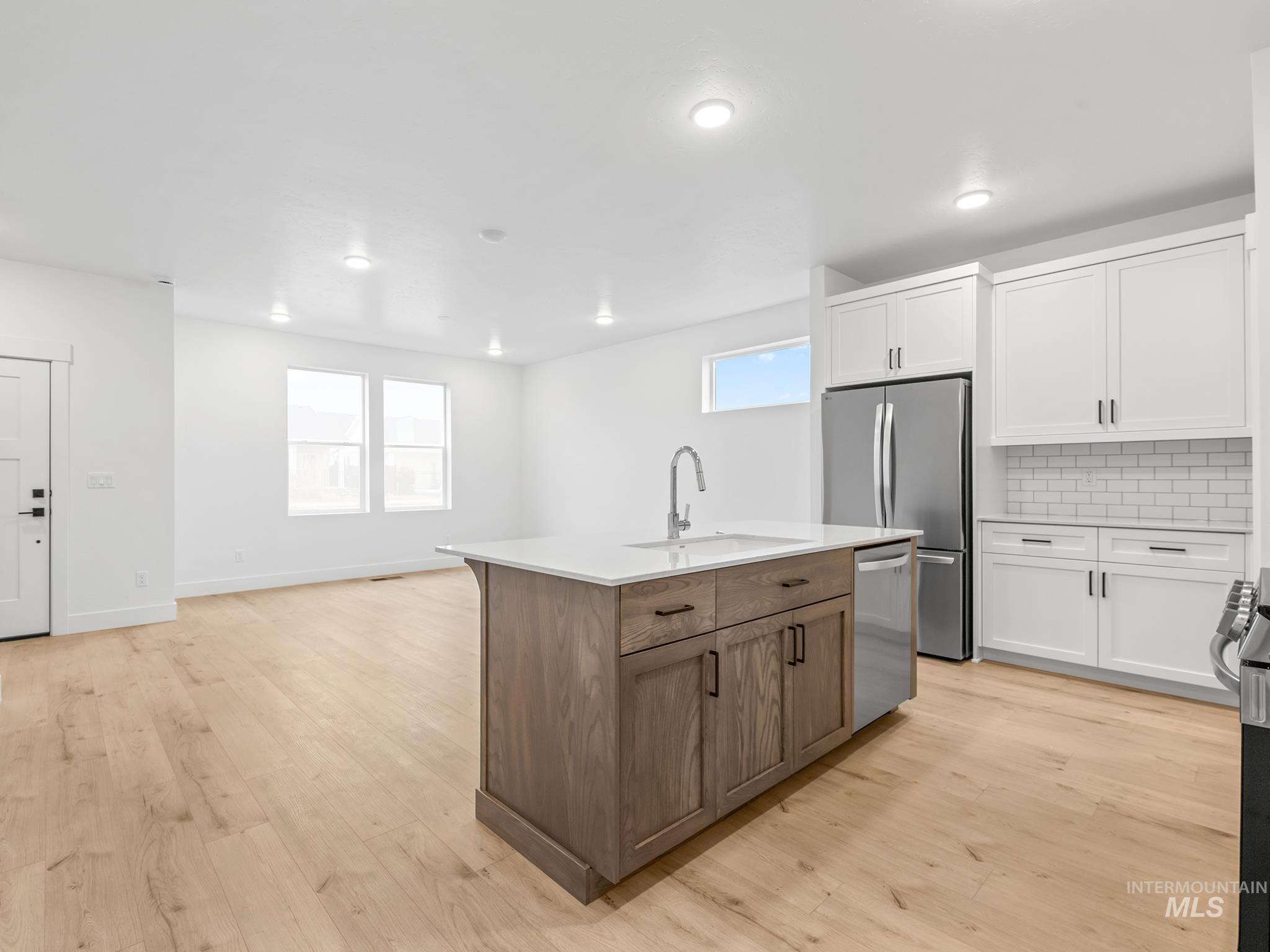 6369 South Sachet Avenue Meridian, ID 83642 - Photo 4 of 13 Dual tone kitchen with a center island with sink, backsplash, two tone cabinets, stainless steel appliances, and light wood-style flooring
