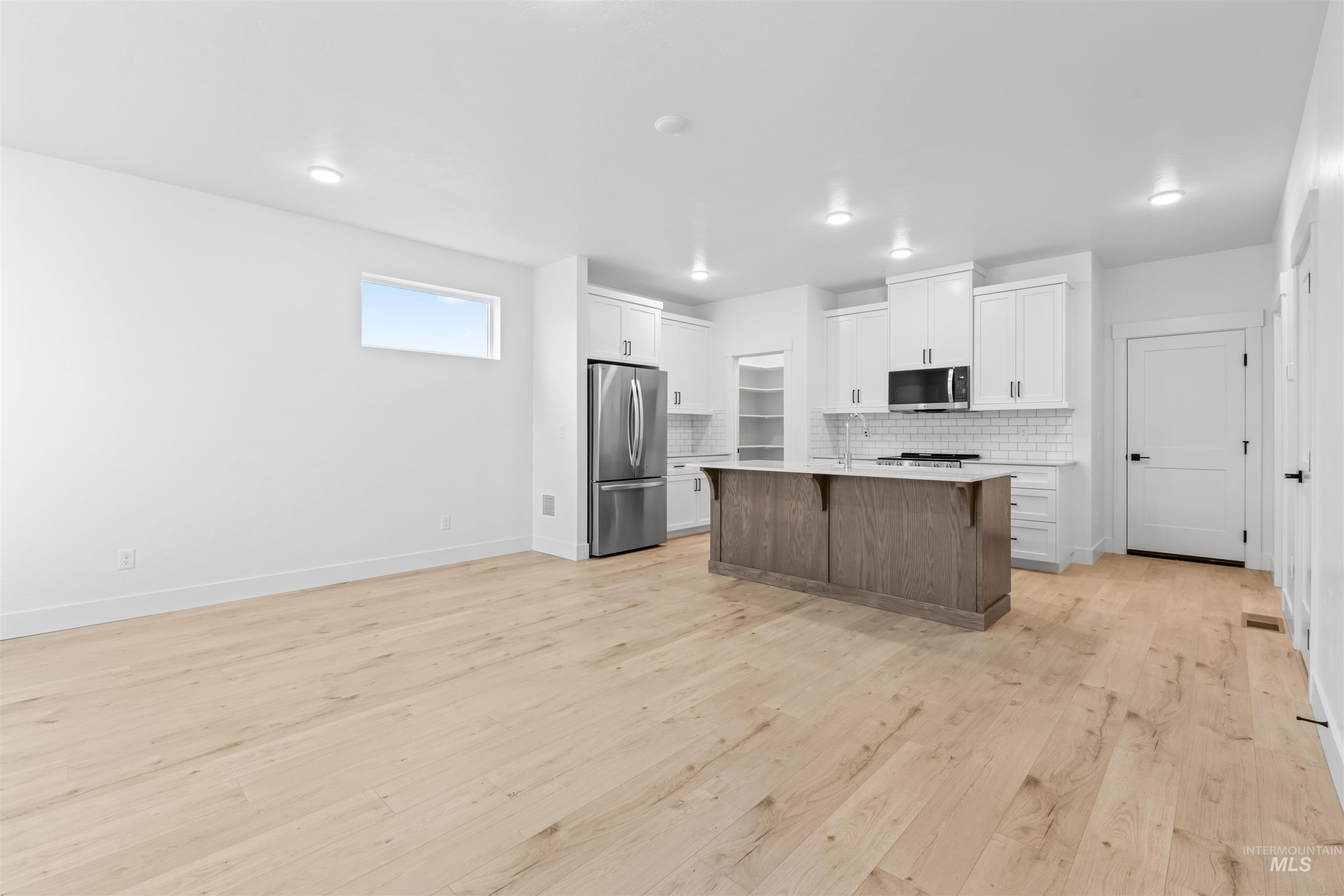 6369 South Sachet Avenue Meridian, ID 83642 - Photo 12 of 13 Two tone kitchen with stainless steel appliances, light wood-style flooring, a kitchen island with sink, open floor plan, and a kitchen breakfast bar