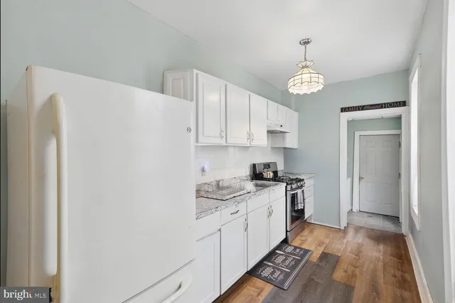 a kitchen with granite countertop a refrigerator a stove and white cabinets with wooden floor