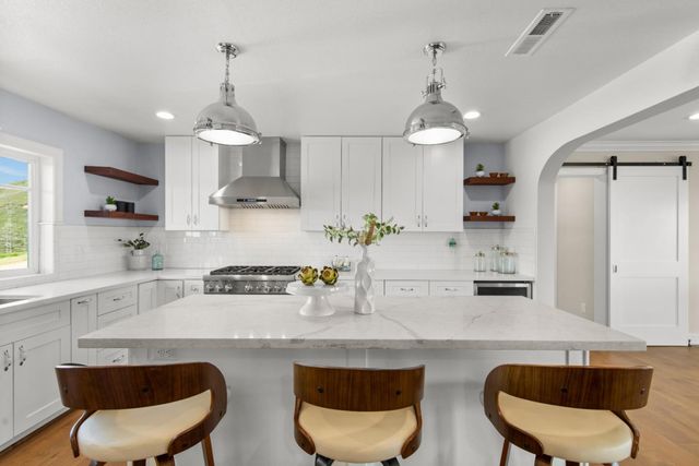 a kitchen with stainless steel appliances granite countertop a sink a stove a refrigerator and chairs