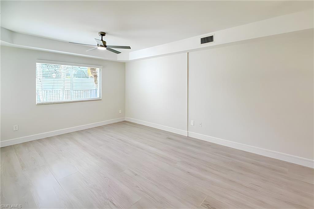 1100 Pine Ridge Road, Unit A106 Naples, FL 34108 - Photo 6 of 27 an empty room with wooden floor chandelier fan and windows