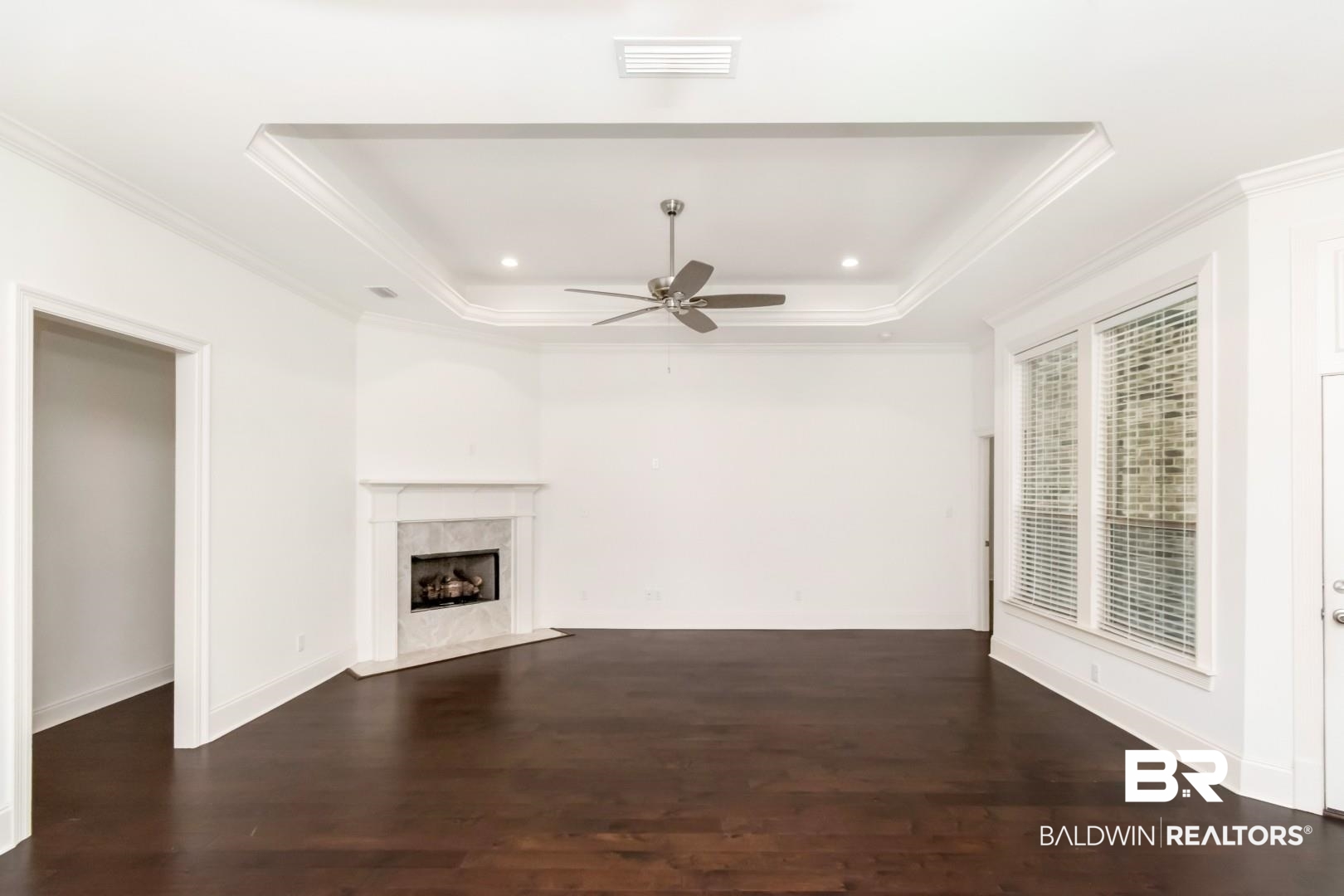 3528 Rue Royal Mobile, AL 36693 - Photo 20 of 53 Spacious interior featuring dark wood-finish flooring, a tray ceiling with recessed lighting and a ceiling fan, and a fireplace with a white mantel and light-toned tile surround