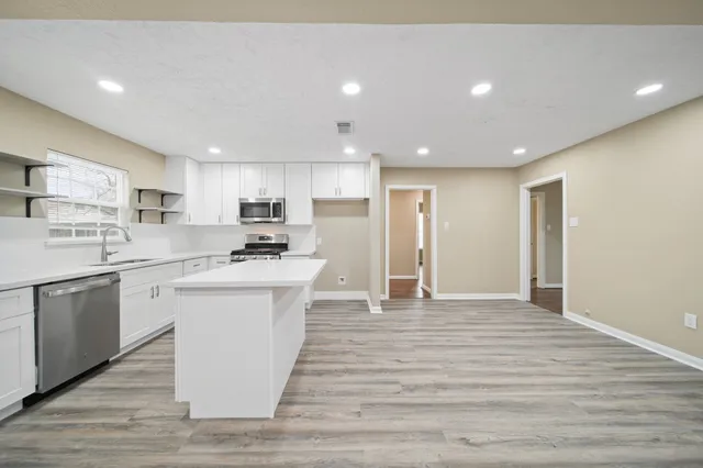 a kitchen with stainless steel appliances granite countertop a stove top oven a sink dishwasher and a refrigerator with wooden floor