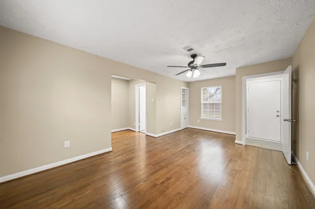 an empty room with wooden floor chandelier fan and windows