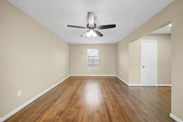 an empty room with wooden floor chandelier fan and windows