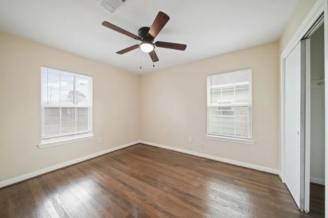 an empty room with wooden floor fan and windows