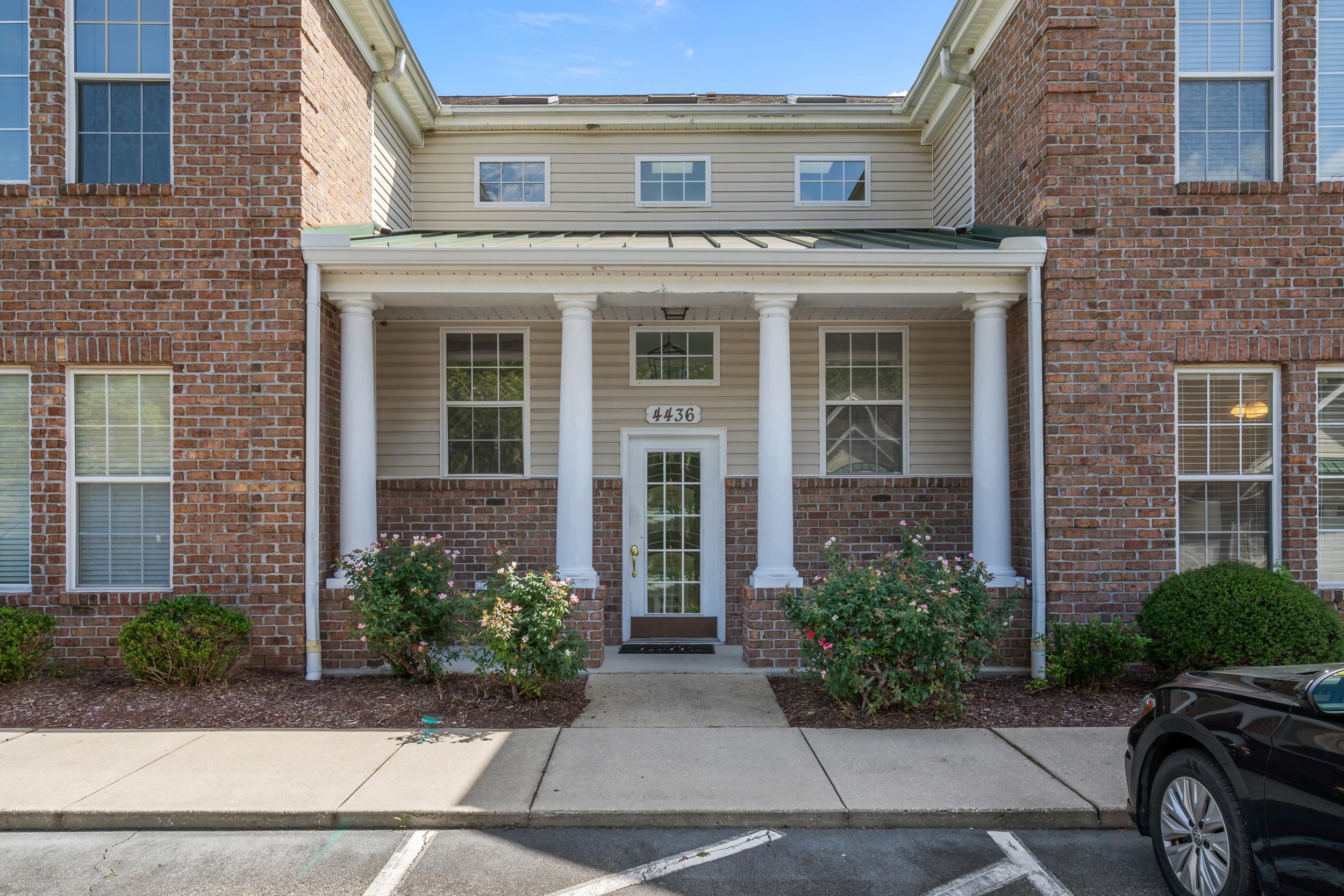View of exterior entry featuring a porch, uncovered parking, and brick siding