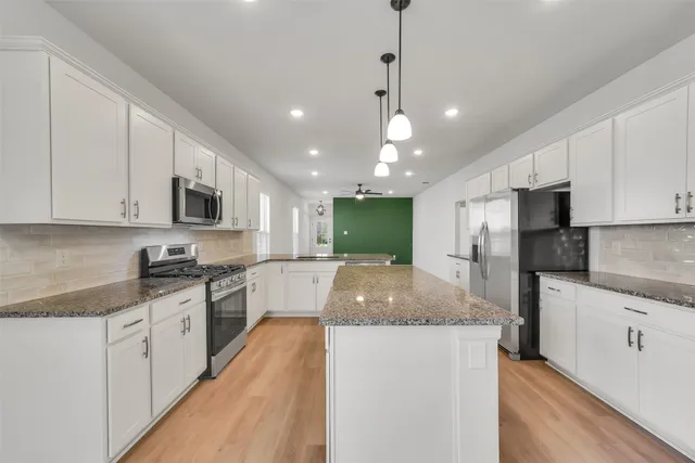 a large kitchen with stainless steel appliances kitchen island granite countertop a stove a sink a refrigerator and white cabinets with wooden floor