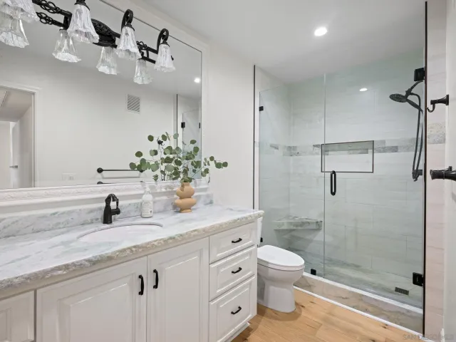 a bathroom with a granite countertop sink a toilet a mirror and shower