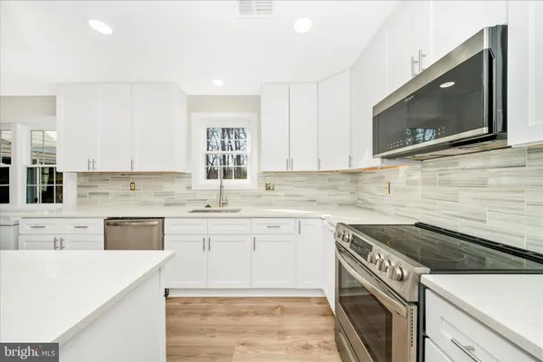 a large kitchen with kitchen island a stove a sink dishwasher a refrigerator and white cabinets with wooden floor