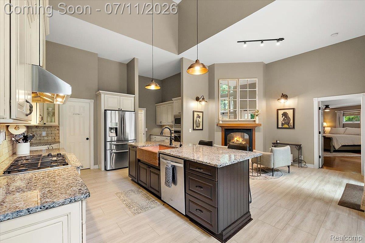 4219 Gardner Road Metamora, MI 48455 - Photo 13 of 87 Kitchen and living area featuring a central island with a copper farmhouse sink, granite countertops, stainless steel appliances, a gas range with a stainless steel vent hood, and a fireplace with a wood mantle