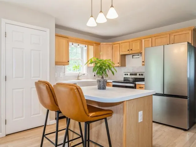 a kitchen with stainless steel appliances granite countertop a refrigerator a sink a stove a dining table and chairs with wooden floor