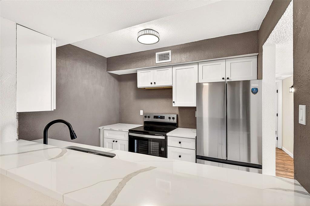 11460 Audelia Road, Unit 287 Dallas, TX 75243 - Photo 11 of 39 Kitchen featuring a textured wall, white cabinets, appliances with stainless steel finishes, light stone countertops, and a peninsula