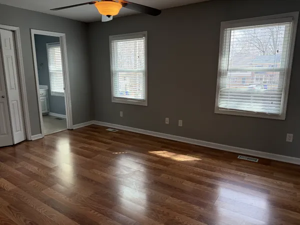 an empty room with wooden floor fan and windows