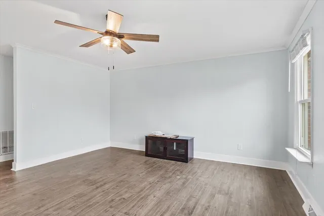 an empty room with wooden floor fan and windows