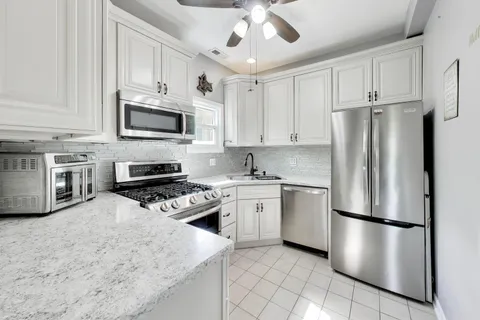 a kitchen with stainless steel appliances granite countertop a refrigerator a stove a microwave oven a sink dishwasher and white cabinets with wooden floor