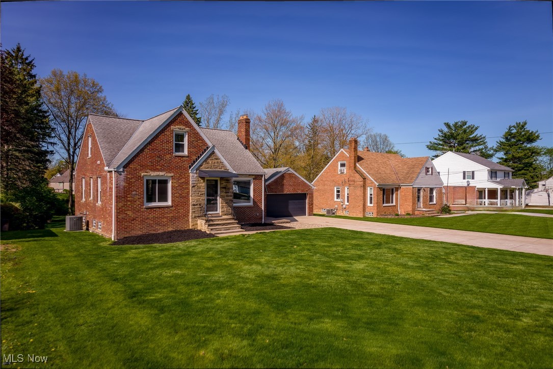 6315 Brookside Road Independence, OH 44131 - Photo 41 of 41 View of front facade featuring a chimney, a detached garage, brick siding, cooling unit, and a front lawn