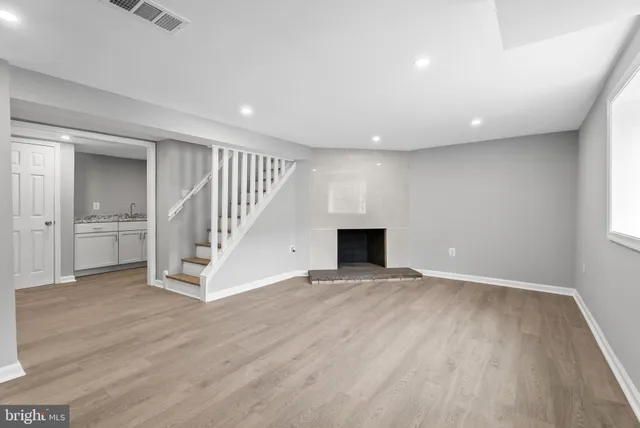 a view of an empty room with wooden floor kitchen and a window