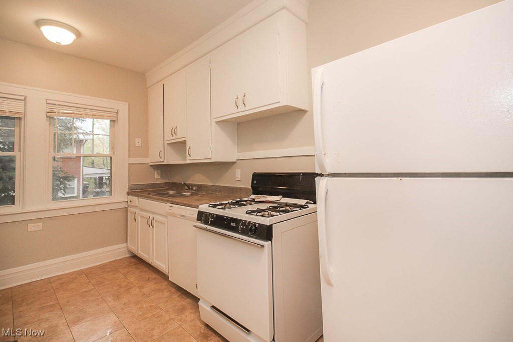 3085 Somerton Road Cleveland, OH 44118 - Photo 8 of 16 Kitchen featuring dark countertops, white cabinetry, white appliances, light tile patterned floors, and baseboards