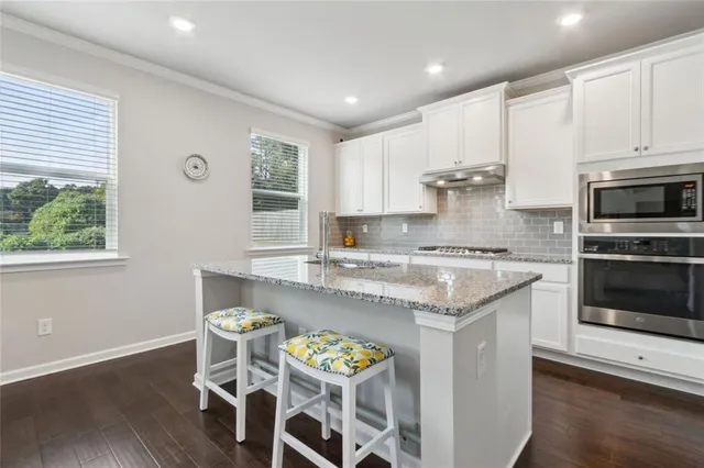 a kitchen with granite countertop stainless steel appliances a stove a sink a microwave a refrigerator and white cabinets with wooden floor