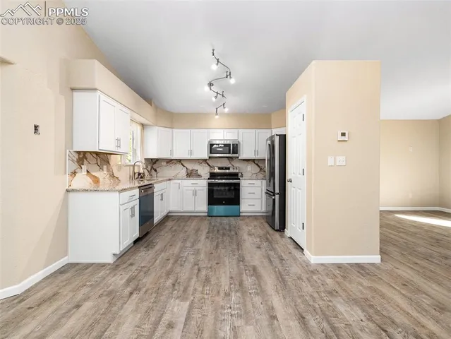 a kitchen with granite countertop a refrigerator oven a sink dishwasher and white cabinets with wooden floor