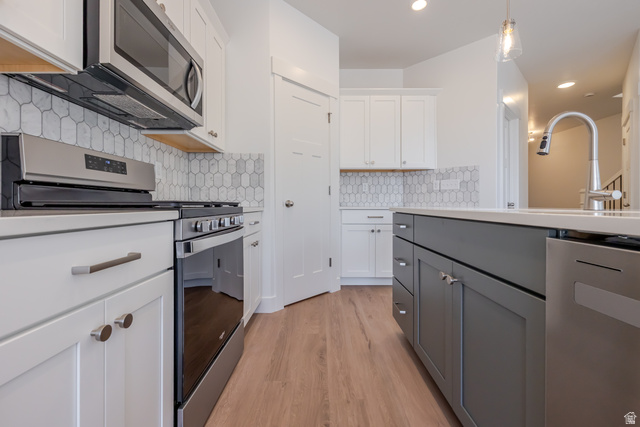 5228 South Acacia Drive, Unit 808 Mapleton, UT 84664 - Photo 11 of 22 Kitchen featuring wood-finish flooring, two-tone cabinetry, stainless steel appliances, a tile backsplash, and a kitchen island with an integrated sink