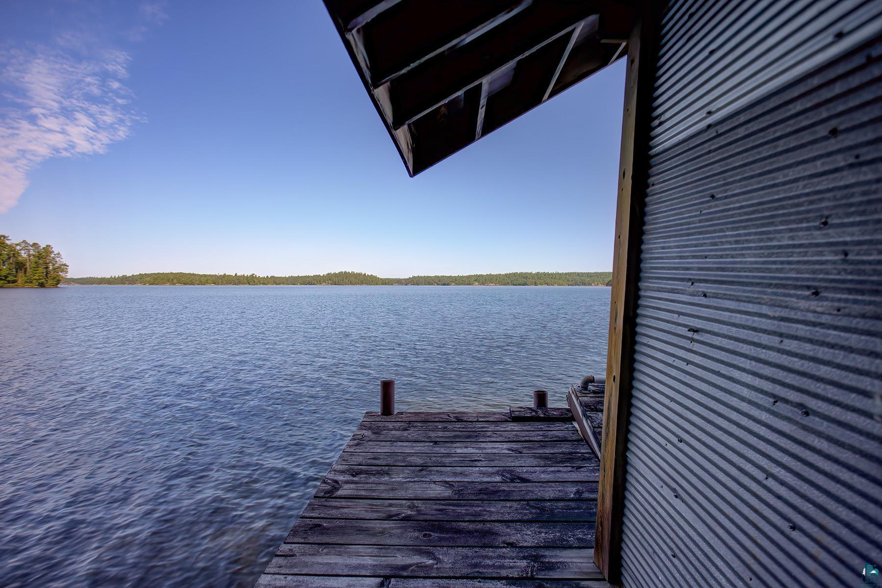 2811 Schaeffer Road Ely, MN 55731 - Photo 29 of 40 Lakefront access featuring a wooden dock, corrugated metal structure, and expansive water frontage with a tree-lined horizon