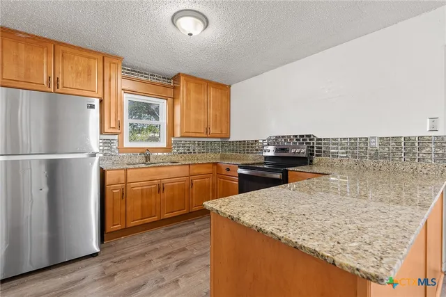 a kitchen with granite countertop a refrigerator and wooden cabinets