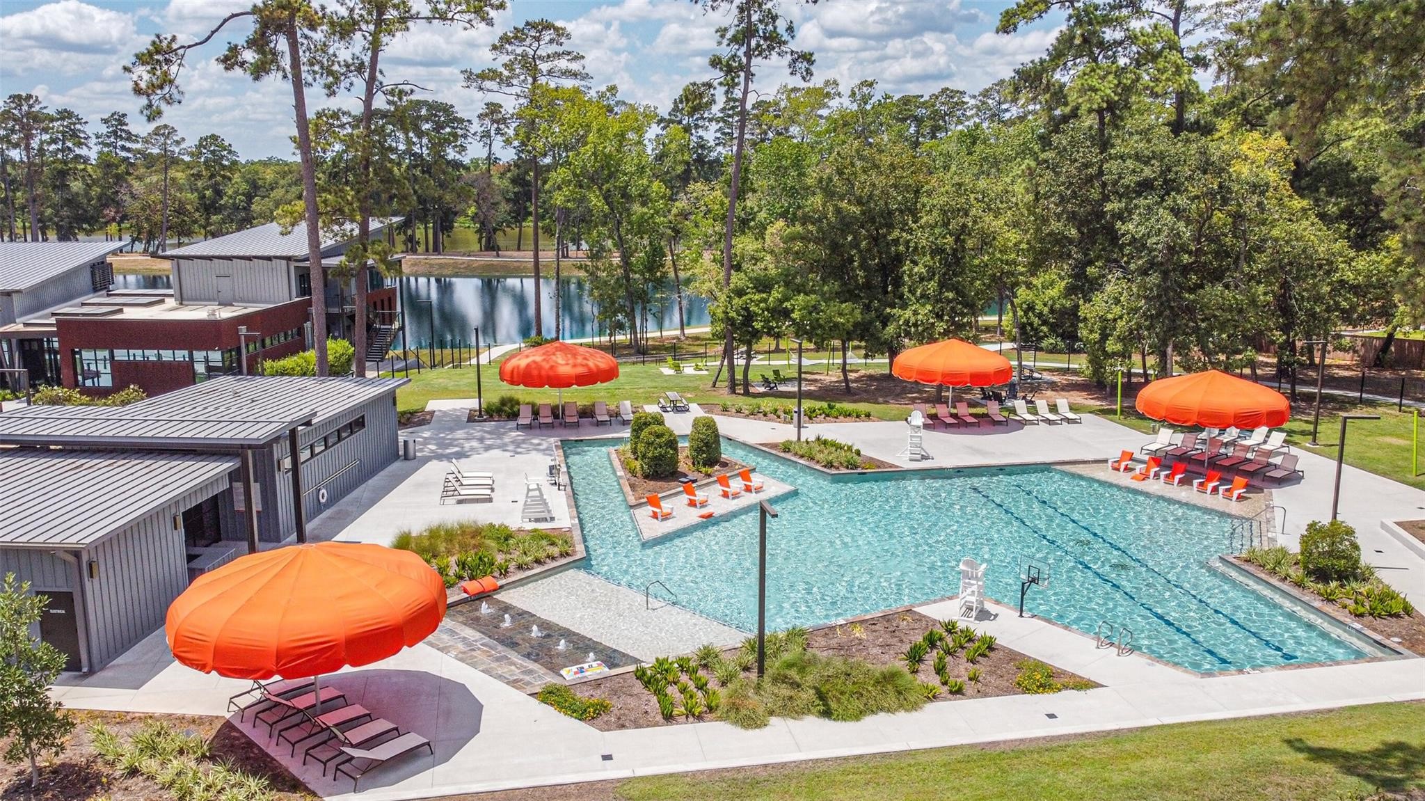 718 Santa Elena Trail Conroe, TX 77304 - Photo 26 of 29 Discover a serene oasis where luxury meets nature with a sparkling pool, vibrant orange umbrellas, and lush greenery, offering the perfect blend of relaxation and style for your dream home.