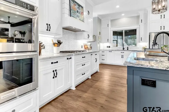 a kitchen with stainless steel appliances kitchen island granite countertop a sink a stove a refrigerator and island with wooden floor