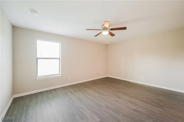 an empty room with wooden floor ceiling fan and window