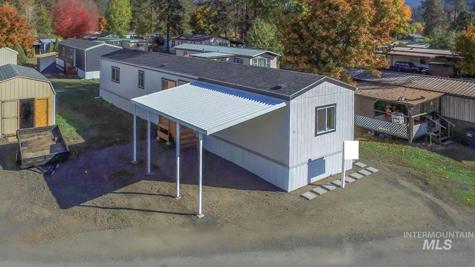 10 Kamloop Lane Orofino, ID 83544 - Photo 1 of 17 Manufactured home featuring white vertical siding with dark trim accents, a covered carport, and a dark shingle roof