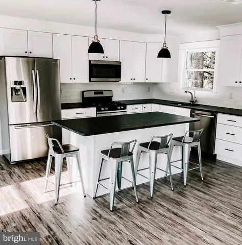 a kitchen with stainless steel appliances granite countertop a stove a refrigerator a microwave a sink and white cabinets with wooden floor